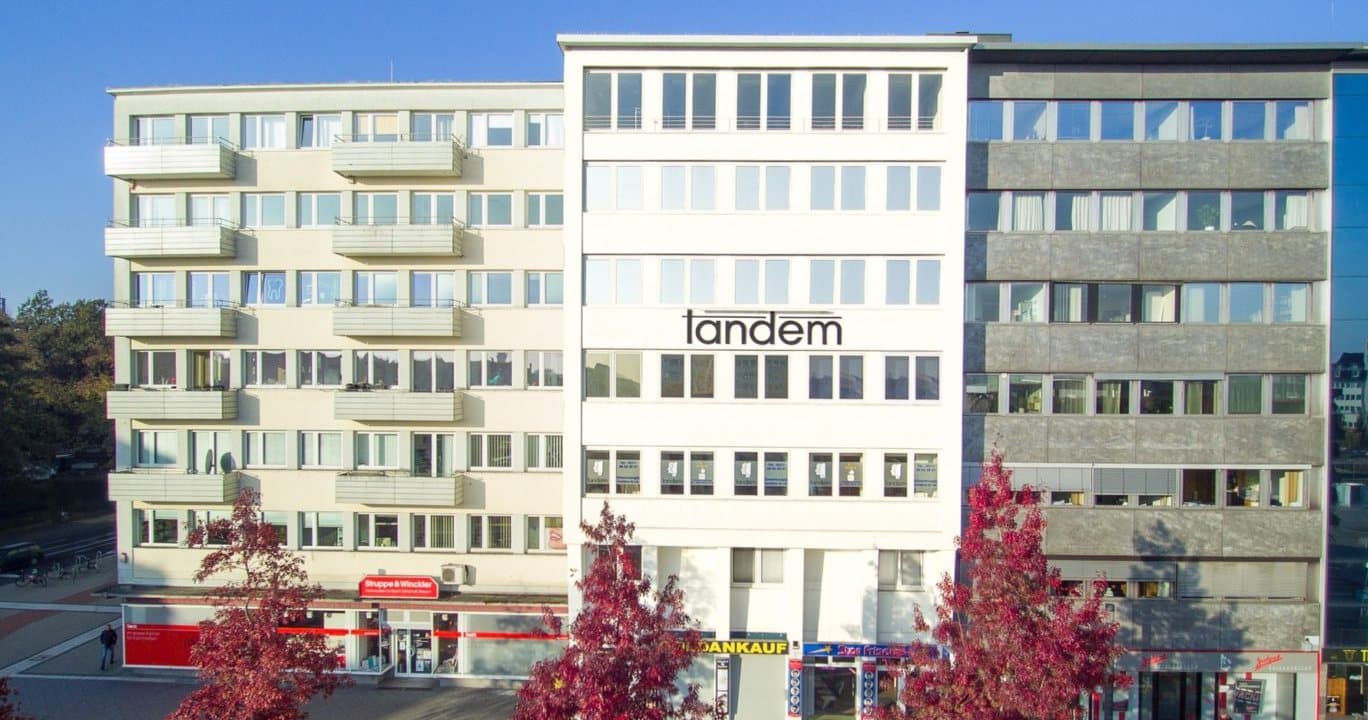 Office building with the tandem lettering on its façade, trees with red autumn leaves in front